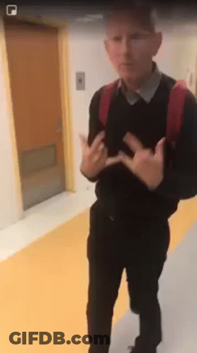 A Man With A Backpack Is Standing In A Hallway With His Hands Outstretched . GIF
