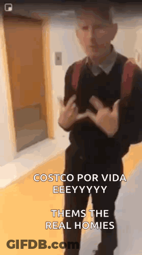 A Man With A Backpack Is Standing In Front Of A Door And Giving The Middle Finger . GIF