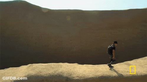A Man With A Backpack Is Walking Across A Desert Landscape GIF