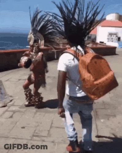 A Man With A Backpack Is Walking In Front Of A Native American GIF