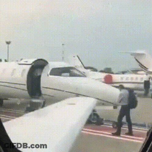 A Man With A Backpack Is Walking Towards A White Airplane . GIF