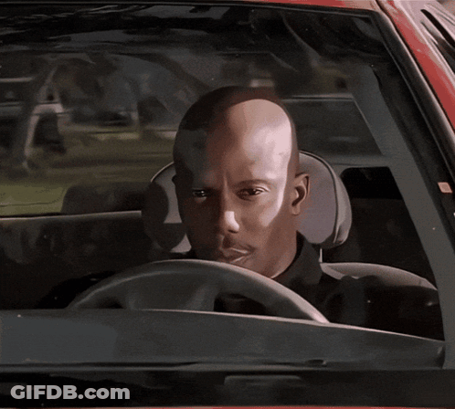 A Man With A Bald Head Is Driving A Car And Looking At The Camera GIF