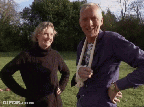 A Man With A Bandage On His Arm Stands Next To A Woman In A Black Sweater GIF