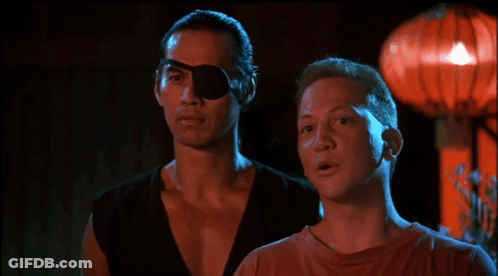 A Man With A Bandage On His Eye Is Touching Another Man 'S Face In A Dark Room GIF