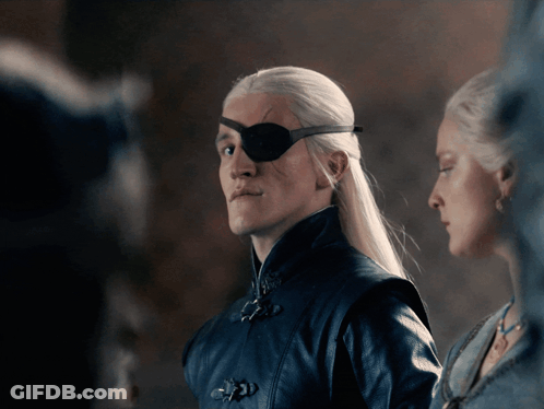 A Man With A Bandage On His Eye Stands Next To A Woman GIF