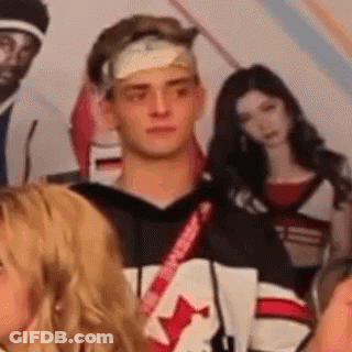 A Man With A Bandage On His Head Is Standing In Front Of A Group Of People . GIF