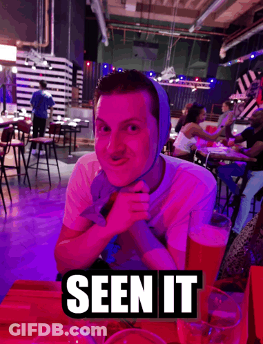 A Man With A Bandage On His Head Sits At A Table With A Sign That Says Seen It On It GIF