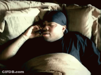 A Man With A Bandana On His Head Is Laying In Bed Talking On A Cell Phone GIF