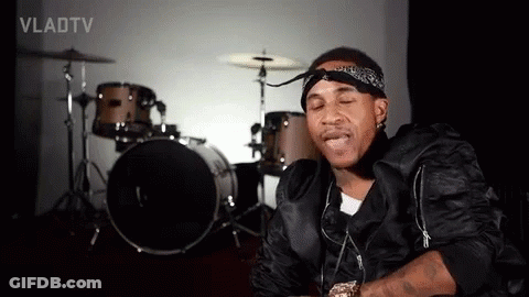 A Man With A Bandana On His Head Is Sitting In Front Of A Drum Set In A Room . GIF