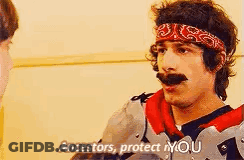 A Man With A Bandana On His Head Is Talking To Another Man While Wearing Armor . GIF