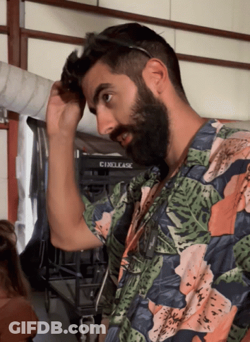 A Man With A Beard Adjusts His Sunglasses In Front Of A Cinelease Sign GIF