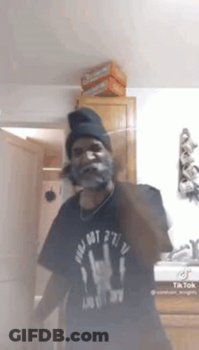 A Man With A Beard And A Beanie Is Standing In A Room . GIF