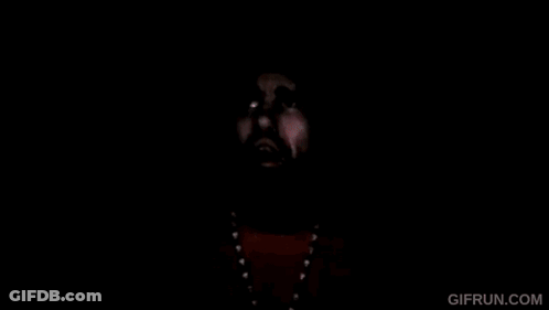 A Man With A Beard And A Beanie Is Wearing A Yellow Shirt And Necklace . GIF