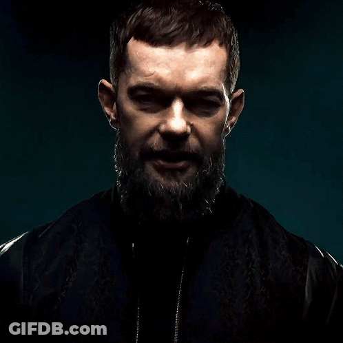 A Man With A Beard And A Black Jacket Is Looking At The Camera GIF