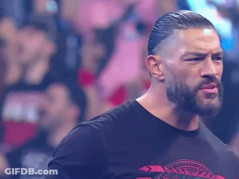 A Man With A Beard And A Black Shirt Is Standing In Front Of A Crowd And Making A Funny Face . GIF