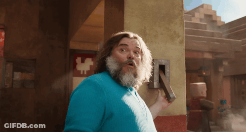 A Man With A Beard And A Blue Shirt Is Holding A Block GIF