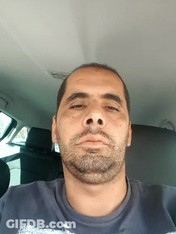 A Man With A Beard And A Blue Shirt Is Looking Down GIF