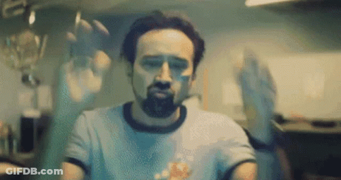 A Man With A Beard And A Blue Shirt Is Sitting In A Kitchen . GIF