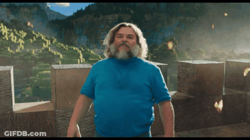 A Man With A Beard And A Blue Shirt Stands In Front Of A Mountain GIF