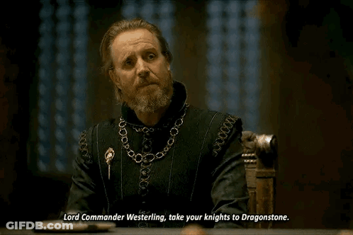 A Man With A Beard And A Chain Around His Neck Is Sitting At A Table And Talking To Someone . GIF