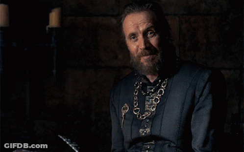 A Man With A Beard And A Chain Around His Neck Is Sitting In A Dark Room . GIF