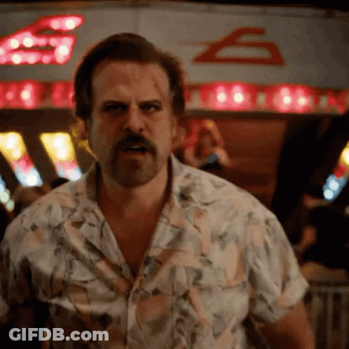 A Man With A Beard And A Floral Shirt Is Standing In Front Of A Sign That Says ' S ' On It GIF