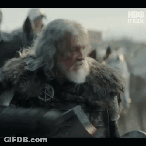 A Man With A Beard And A Fur Coat Is Holding A Sword In His Hand . GIF