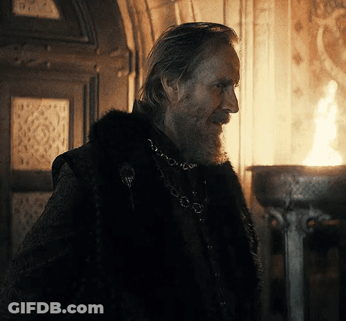 A Man With A Beard And A Fur Coat Is Standing In Front Of A Fire GIF