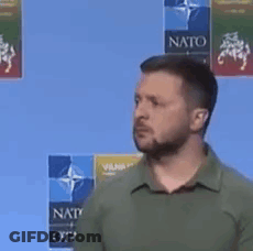 A Man With A Beard And A Green Shirt Is Standing In Front Of A Blue Background . GIF