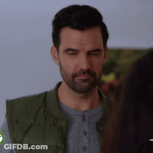 A Man With A Beard And A Green Vest Is Making A Funny Face . GIF
