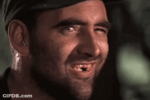 A Man With A Beard And A Hat Is Smiling With A Hole In His Mouth . GIF