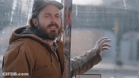 A Man With A Beard And A Hat Is Standing In Front Of A Glass Door . GIF