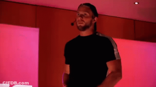 A Man With A Beard And A Hat Is Standing In Front Of A Pink Wall . GIF
