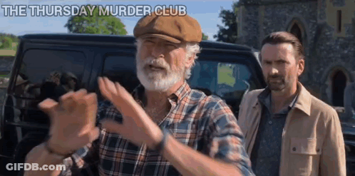 A Man With A Beard And A Hat Is Standing Next To Another Man In Front Of A Van . GIF