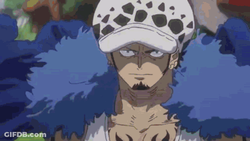 A Man With A Beard And A Hat Is Wearing A Blue Feathered Coat . GIF