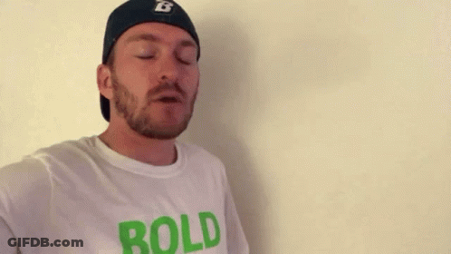 A Man With A Beard And A Hat Is Wearing A White T-Shirt That Says `` Bold '' . GIF