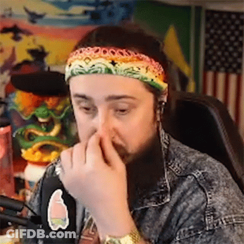 A Man With A Beard And A Headband Is Sitting In Front Of A Microphone And Covering His Nose . GIF