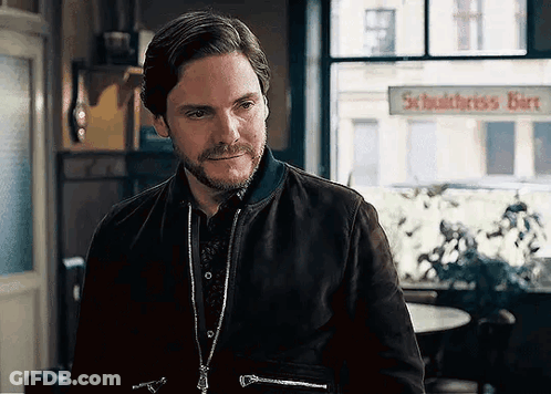 A Man With A Beard And A Jacket Is Standing In Front Of A Window In A Room . GIF