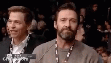 A Man With A Beard And A Lanyard Around His Neck Is Sitting In A Crowd Watching A Boxing Match . GIF
