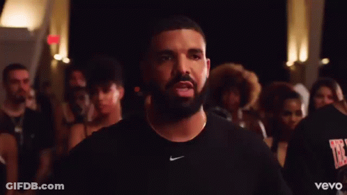 A Man With A Beard And A Nike Shirt Is Standing In Front Of A Crowd Of People . GIF