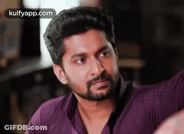 A Man With A Beard And A Purple Shirt Is Looking At The Camera . GIF