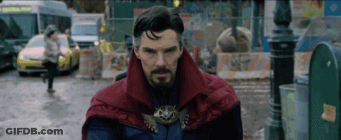 A Man With A Beard And A Red Cape Is Standing In A Street . GIF