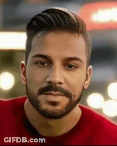 A Man With A Beard And A Red Shirt Looks At The Camera GIF