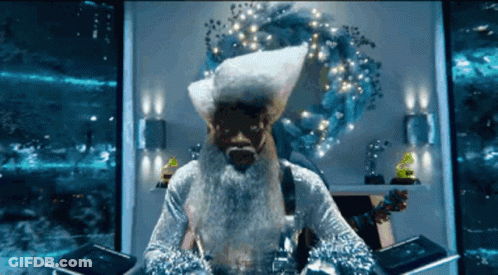 A Man With A Beard And A Santa Hat Is Sitting In Front Of A Wreath GIF