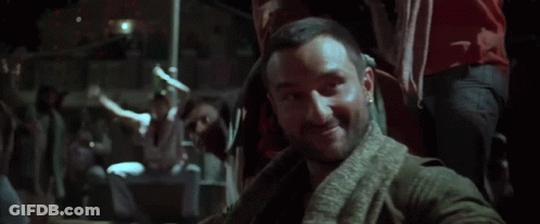 A Man With A Beard And A Scarf Around His Neck Is Standing In The Dark GIF