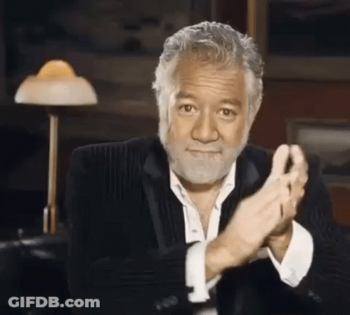 A Man With A Beard And A Suit Is Clapping His Hands In A Room . GIF