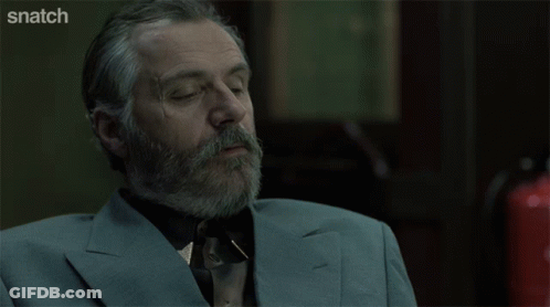 A Man With A Beard And A Suit Is Sitting In Front Of A Screen That Says Snatch GIF