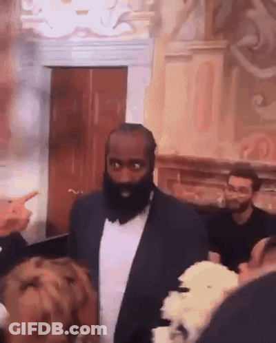 A Man With A Beard And A Suit Is Standing In A Room With People . GIF