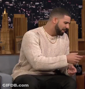 A Man With A Beard And A Sweater Is Sitting On A Couch . GIF