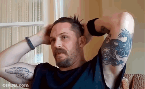 A Man With A Beard And A Tattoo On His Arm Is Holding His Hair In His Hands . GIF